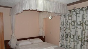 A bedroom with a four-poster bed, a nightstand, and a window with patterned curtains. - Easy Sleep Guesthouse (Kitale)