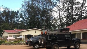 A black SUV parked in front of a building with a red roof, a paved driveway, and a small garden area with umbrellas. - Easy Sleep Guesthouse (Kitale)