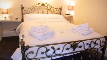 A neatly made bed with white linens and towels, a decorative metal headboard, bedside lamps, and a small bedside table with a tissue box and a phone.