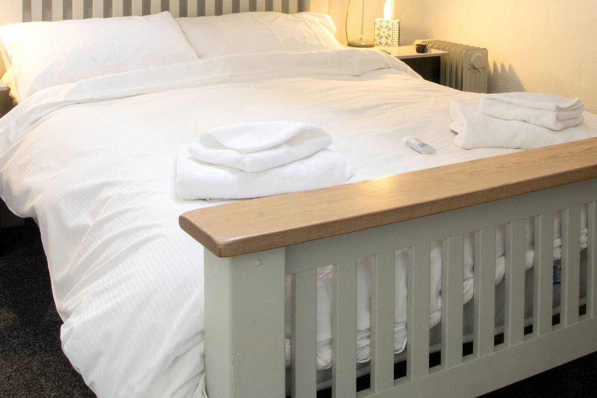 Un lit bien fait, avec du linge de lit blanc, une lampe de chevet et une table de chevet avec une autre lampe.