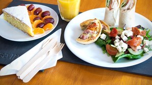 A meal with a slice of cake, a glass of orange juice, and a plate with a wrap, salad, and a small pastry.