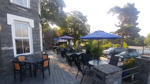 An outdoor patio with stone flooring, black and orange chairs, and blue umbrellas.