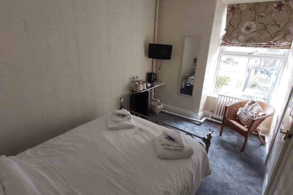 Une chambre d’hôtel avec un lit, un téléviseur fixé au mur, une chaise et une fenêtre donnant sur l’extérieur.