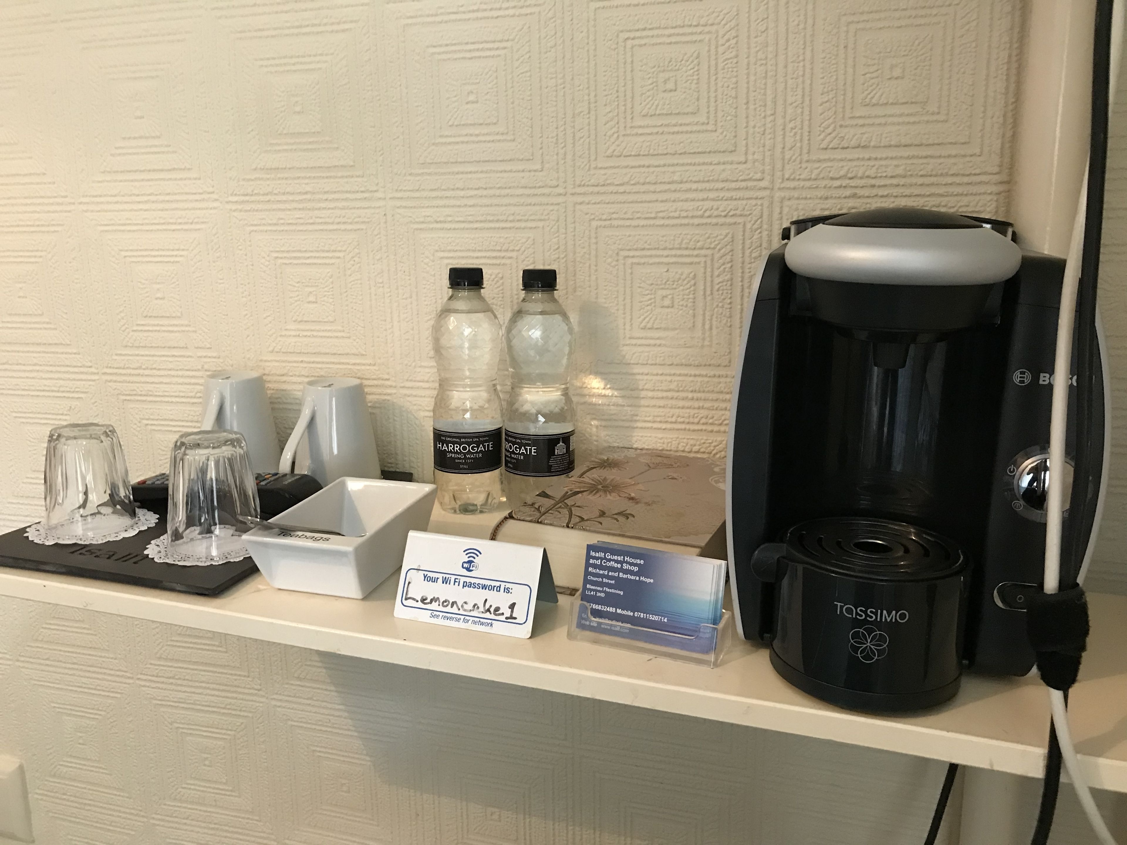 Een hotel receptie met een koffiezetapparaat, waterflesjes en een bord met het Wi-Fi wachtwoord.