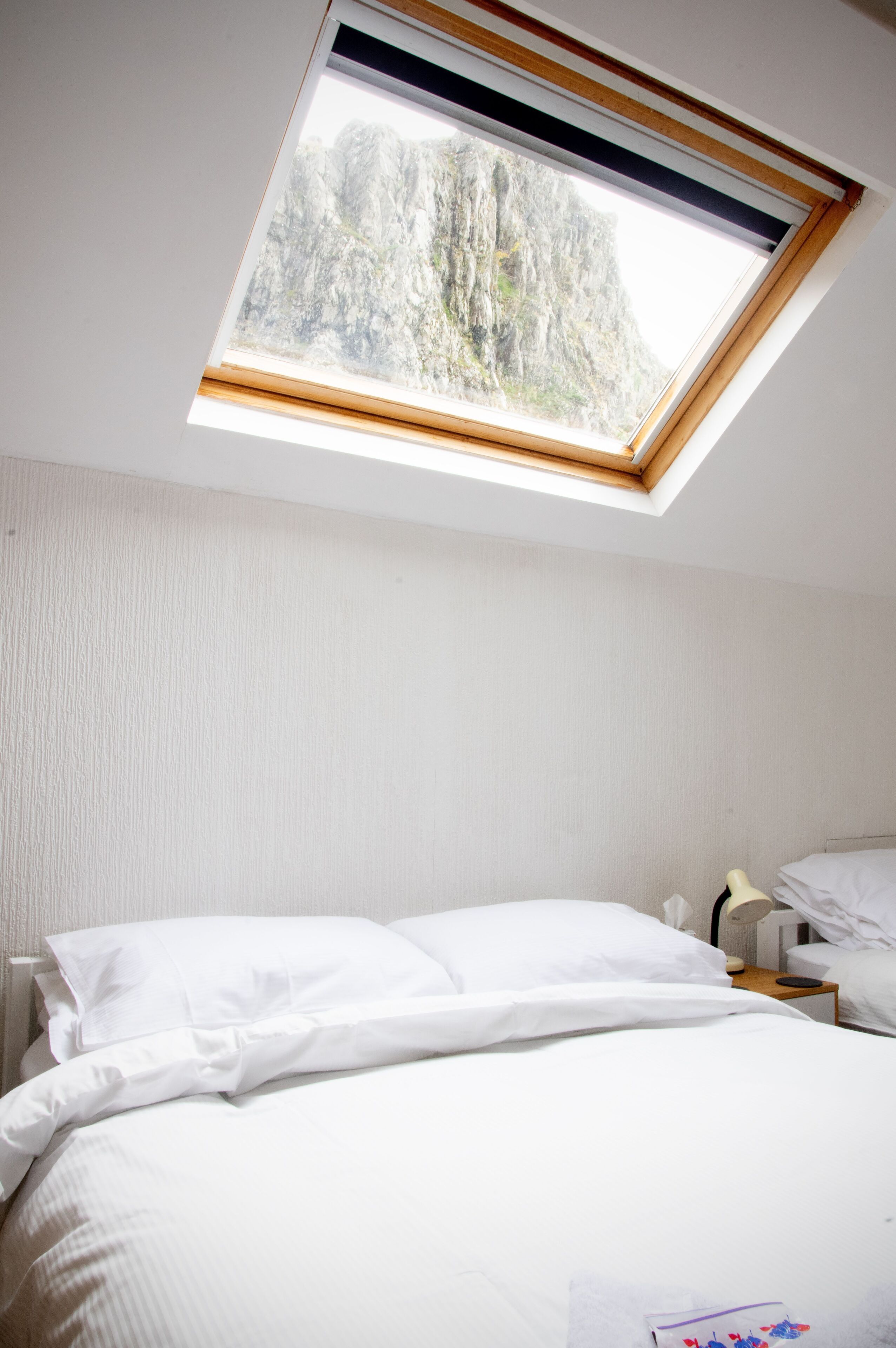 A bedroom with a skylight, a bed, a bedside table, and a nightstand.