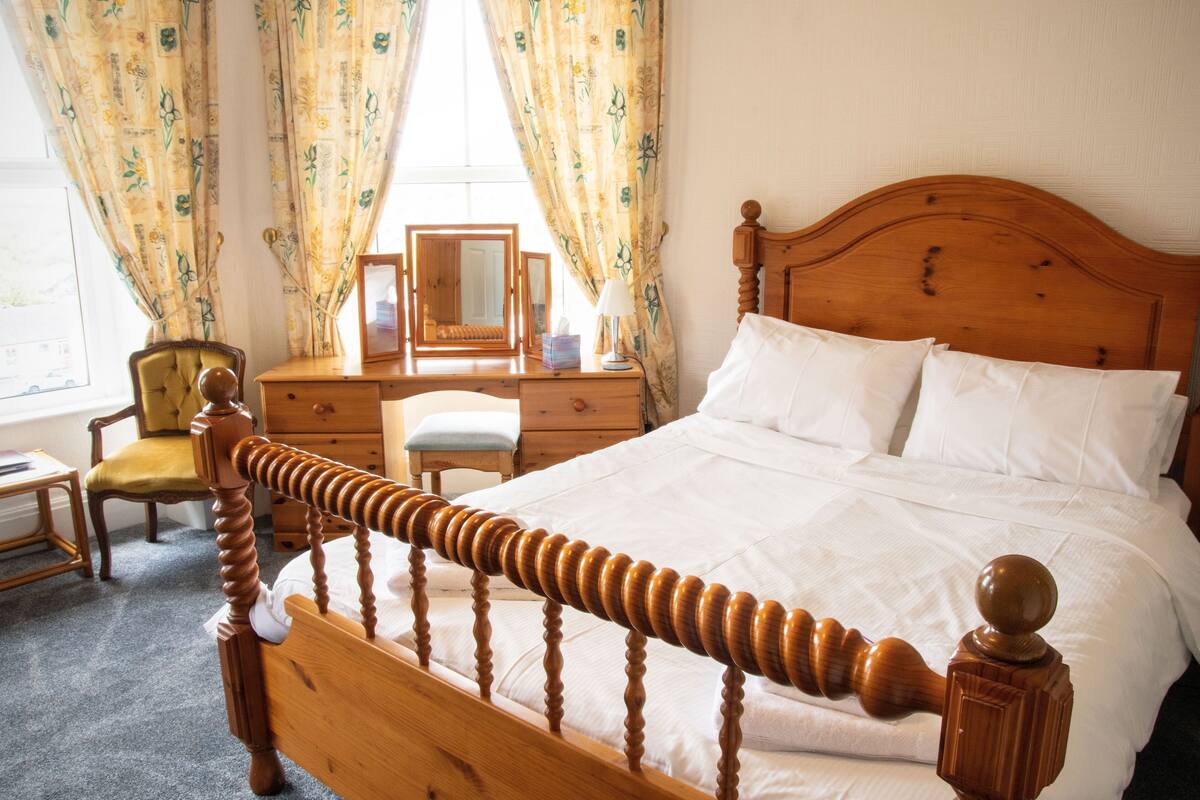 Un lit bien fait, avec une tête de lit en bois, une table de chevet avec une lampe, une chaise et une commode avec un miroir.