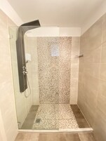 Ένα ντους με γ υάλινο περίβλημα, με πλακάκια στους τοίχους και στο δάπεδο, μια αποσπώμενη κεφαλή ντους και μια γυάλινη πόρτα.