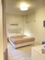 Ένα καλαίσθητο δωμάτιο ξενοδοχείου με ένα κρεβάτι, ένα μικρό κομοδίνο, ένα γραφείο με καρέκλα και μια τηλεόραση τοποθετημένη στον τοίχο.