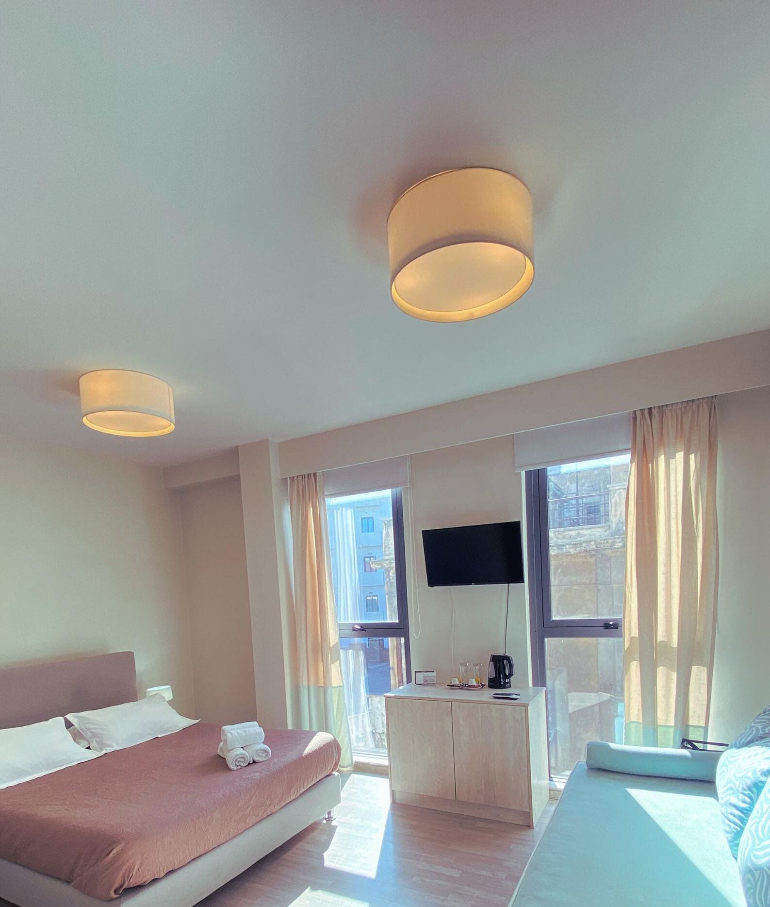 Une chambre d’hôtel équipée d’un lit, d’un bureau, d’une télévision et de grandes fenêtres avec des rideaux.
