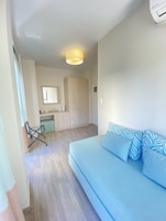 Uma sala de estar moderna com um sofá azul claro, um guarda-roupa de madeira e uma pequena cozinha ao fundo.