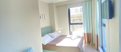 A hotel room with a bed, a sofa, a TV, and a window with curtains.