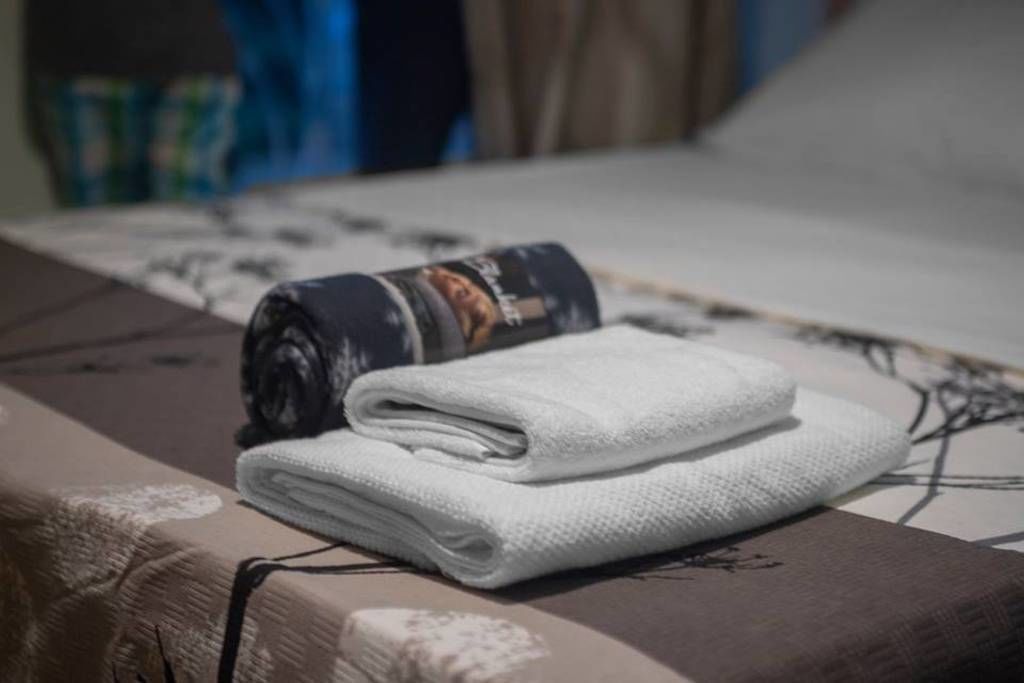 Una toalla blanca doblada con cuidado y una revista enrollada sobre una cama con edredón estampado.