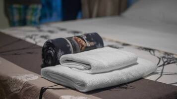 Una toalla blanca doblada con cuidado y una revista enrollada sobre una cama con edredón estampado.