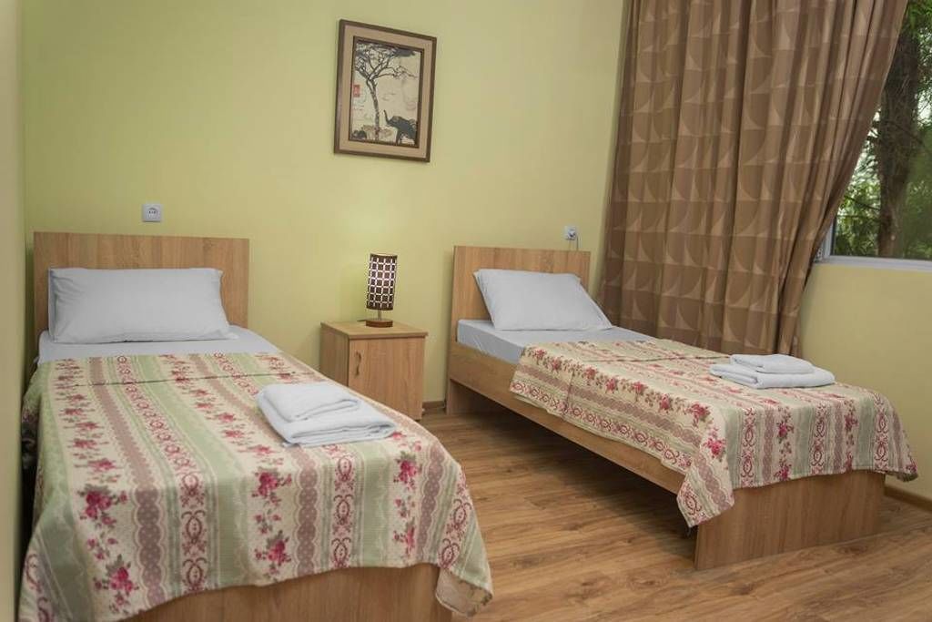 A room with two single beds, wooden headboards, and a small bedside table with a lamp.