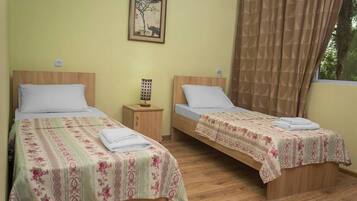 A room with two single beds, wooden headboards, and a small bedside table with a lamp.