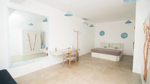 A modern, minimalist bedroom with a large mirror, a bedside table, a chair, and a bed. - Banana Garden Mirissa (Mirissa)