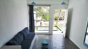 A modern living room with a dark blue sofa, a small table, and a view of a tropical outdoor area through a glass door. - Banana Garden Mirissa (Mirissa)