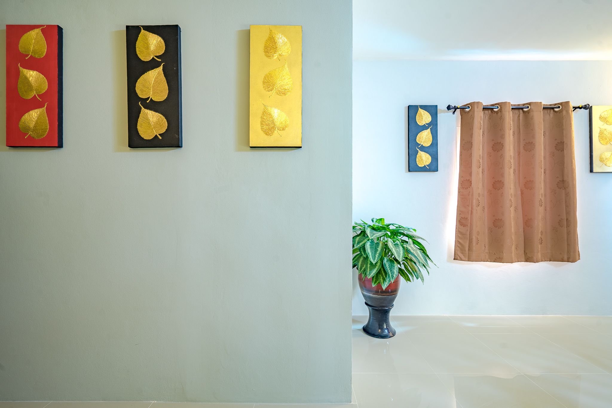 Een kamer met drie kunstwerken in lijsten aan de muur, een potplant en een gordijn.
