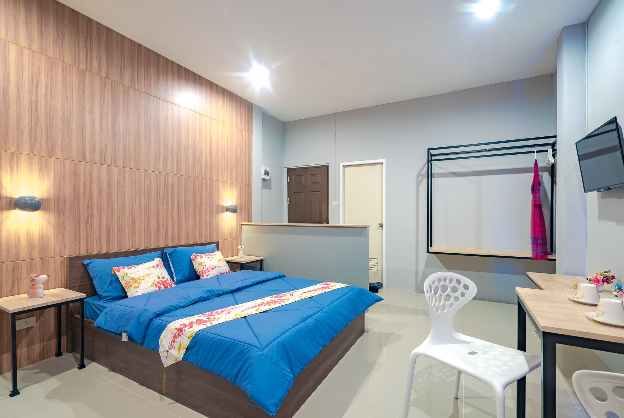 Ein modernes Schlafzimmer mit einer Wand aus Holzpaneelen, einem Bett mit blauer Bettwäsche, einem Nachttisch mit Lampe, einem Schreibtisch mit Stuhl und einem an der Wand montierten Fernseher.