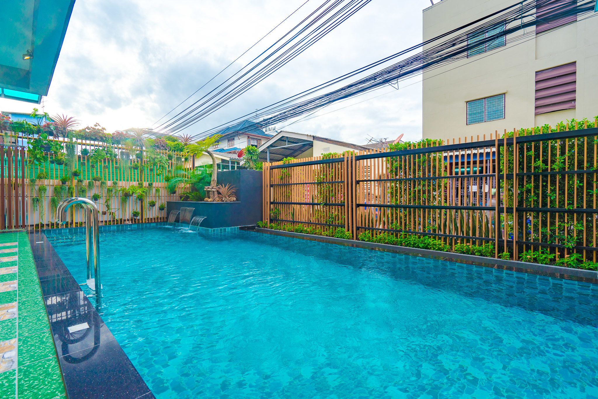 A swimming pool with a wooden fence, a water fountain, and a building with a satellite dish in the background.