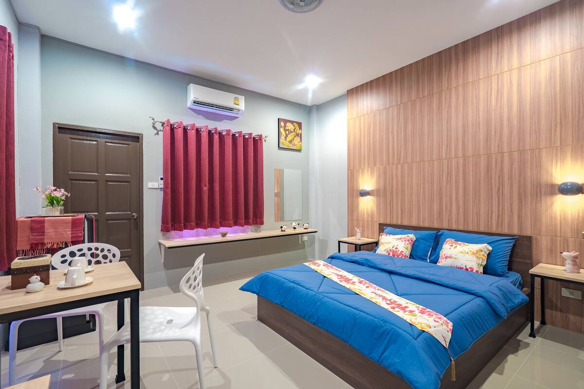 A bedroom with a large bed, a desk with a chair, a vanity with a mirror, and a red curtain.