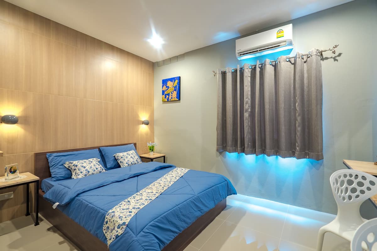 A modern bedroom with a large bed, a bedside table, a small table with a lamp, and a chair.