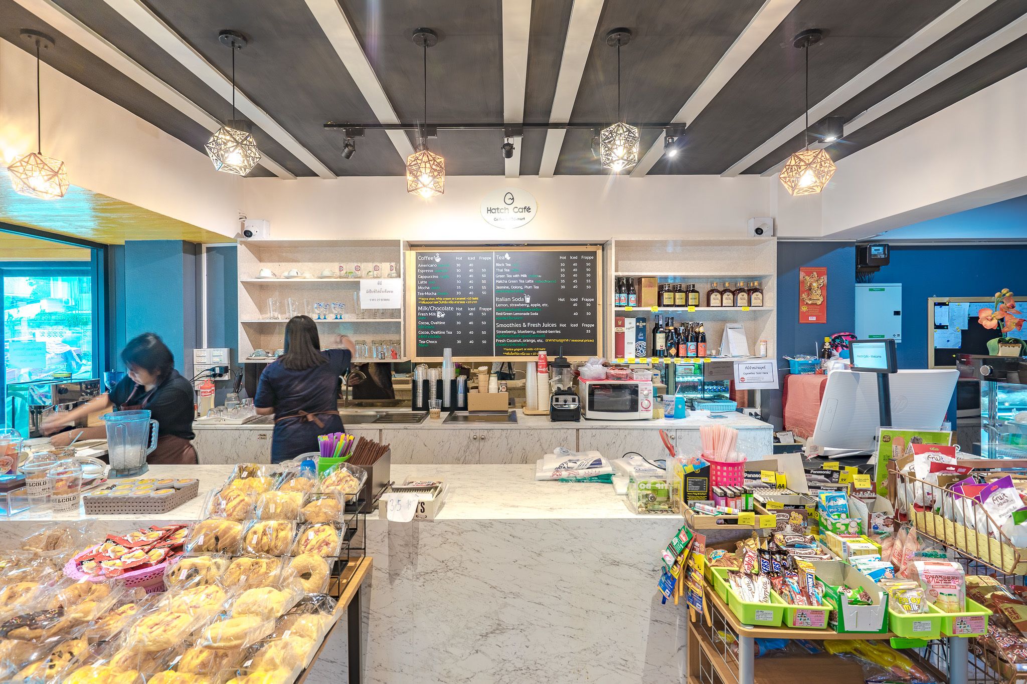 Café com cardápio, máquinas de café e diversos doces e salgados expostos.