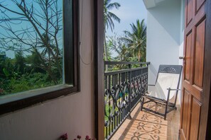 Ein Balkon mit Metallgeländer, einer Holztür und Blick auf Grünflächen und Palmen.