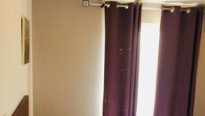 Una habitación de hotel con cama, cortinas y cabecero.