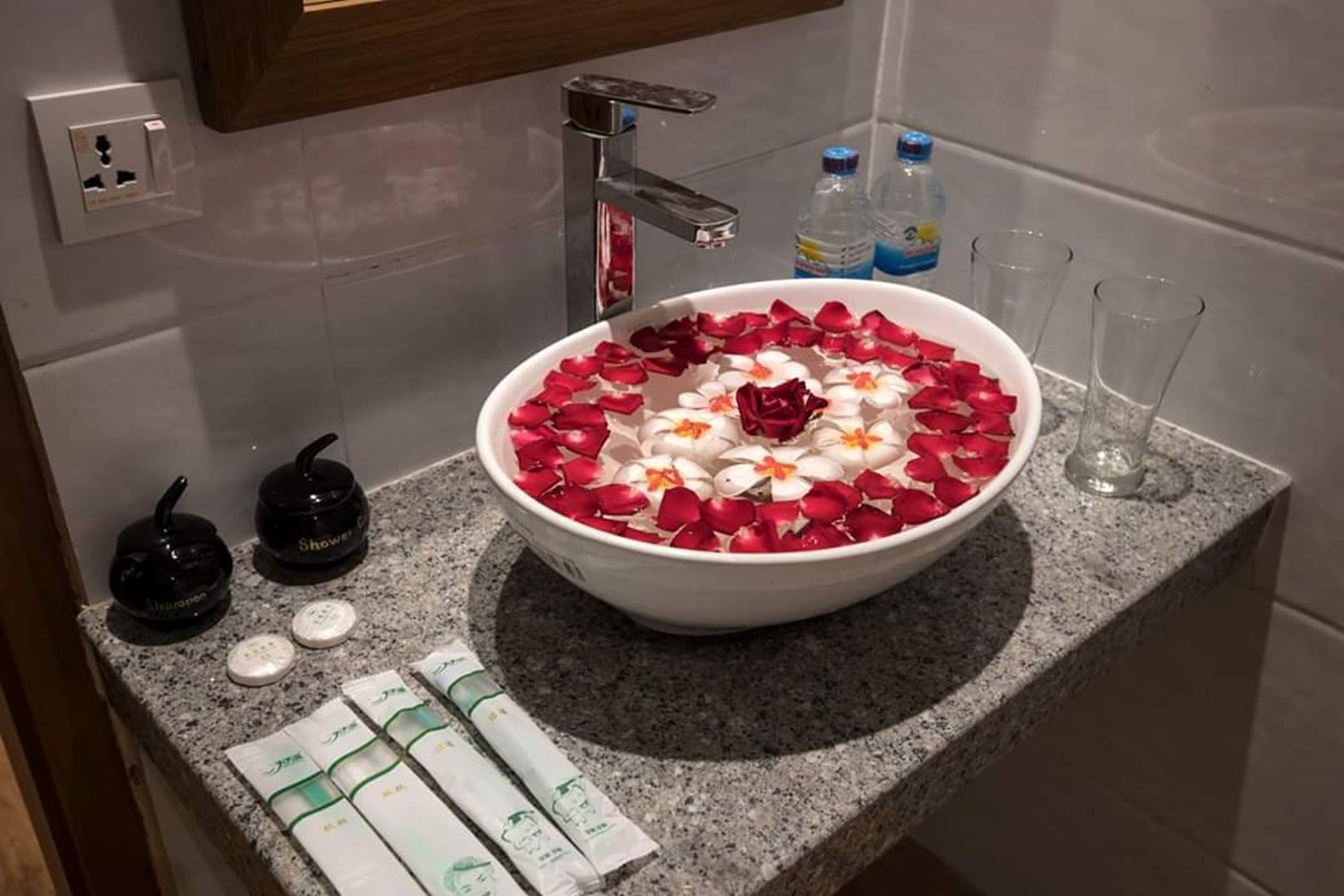 Une salle de bain avec un lavabo blanc, des pétales de rose et des articles de toilette disposés sur le comptoir.