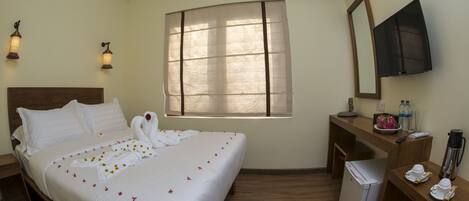 A hotel room with a bed, a desk, a refrigerator, a mirror, and a window with blinds.