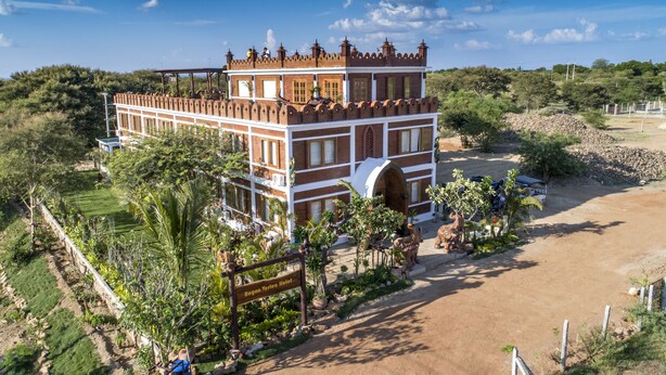 Un edificio grande de varios pisos con un estilo arquitectónico distintivo, rodeado de vegetación exuberante y un cielo despejado.