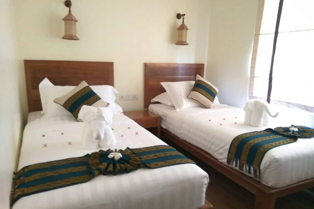 Deux lits jumeaux, joliment préparés, avec des têtes de lit en bois, du linge de lit blanc et des coussins décoratifs.