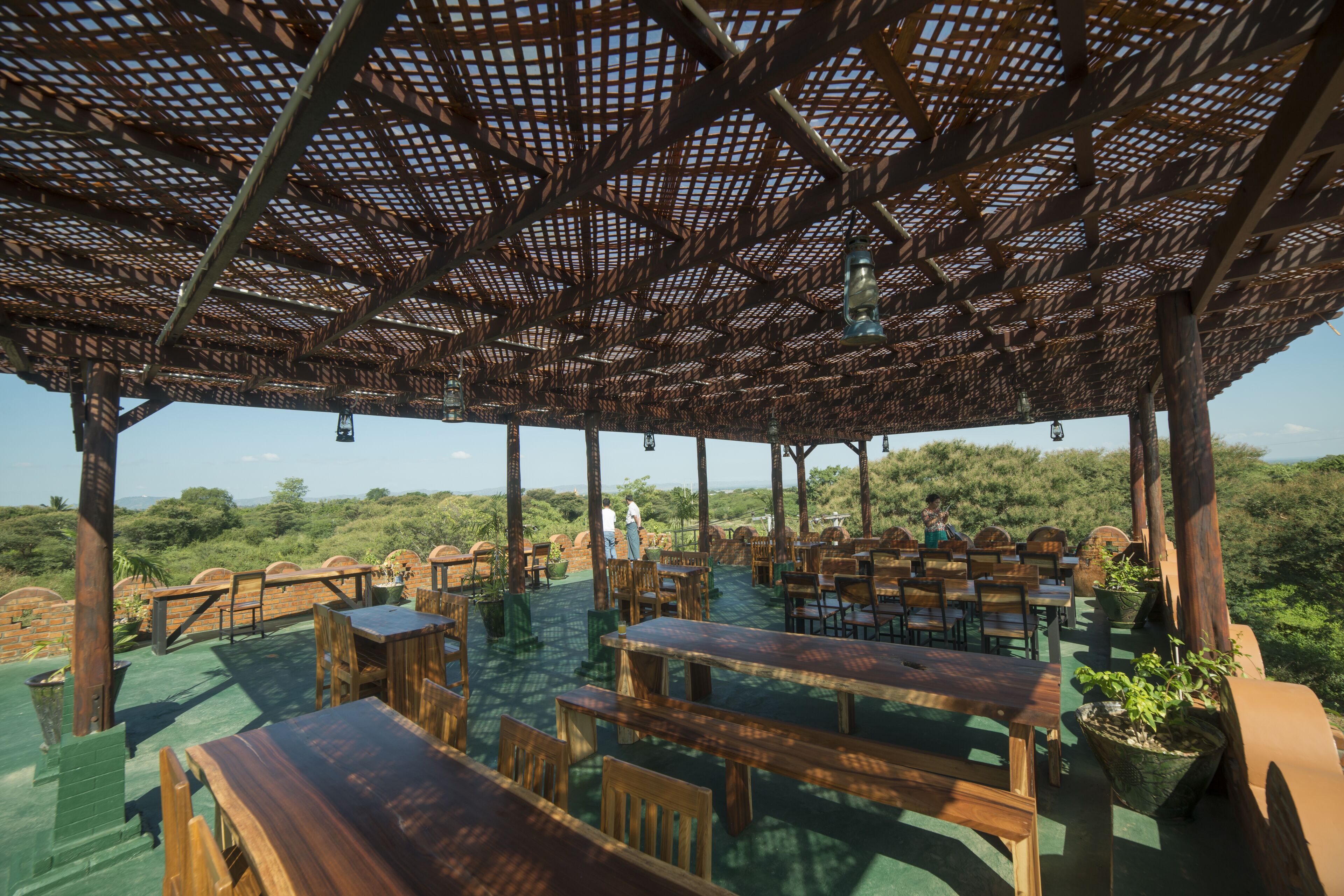 Un espace de restauration en plein air avec des tables et des chaises en bois, une pergola au-dessus et une vue sur le paysage environnant.