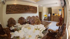 Un área de recepción con un mostrador de madera, un gran panel de madera tallada encima del mostrador y un arreglo floral en primer plano.