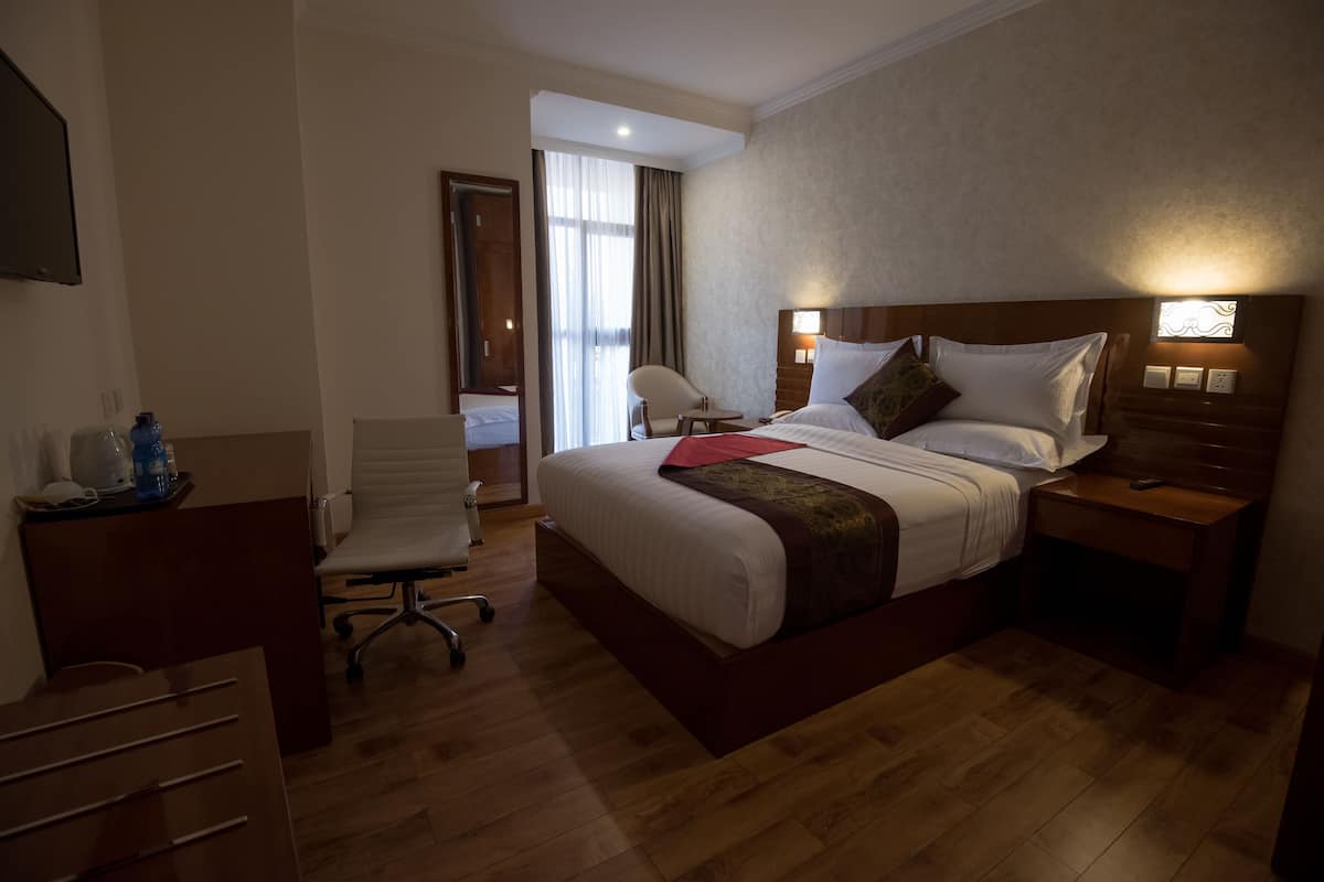 Ein Hotelzimmer mit einem großen Bett, einem Schreibtisch, einem Stuhl und einem Vorhangfenster.
