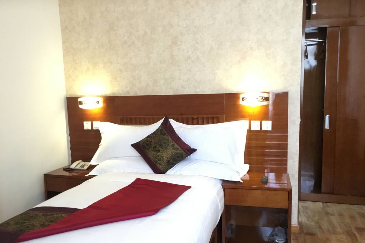 Ein Hotelzimmer mit einem ordentlich bezogenen Bett, zwei Nachttischlampen, einem Holz-Kopfteil und einem Holzschrank.