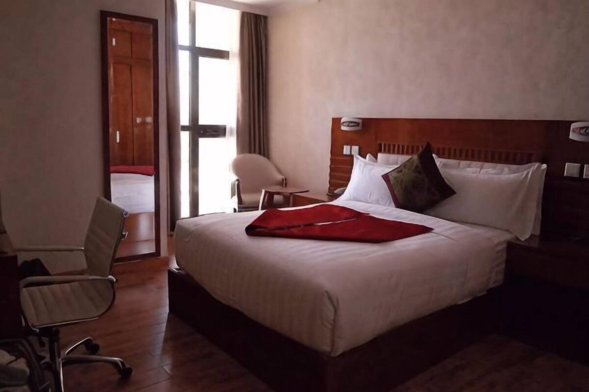 Ein Hotelzimmer mit Bett, Stuhl, Schreibtisch und Blick nach außen.