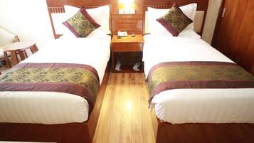 A hotel room with two beds, a wooden nightstand with a phone and a clock, and a small table with chairs.