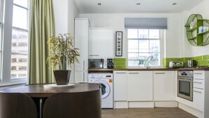 Une cuisine moderne équipée d’un lave-linge, d’un four à micro-ondes et d’une cuisinière. On y trouve une table à manger avec des chaises et une plante en pot.