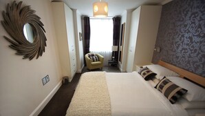 A hotel room with a large bed, a round mirror on the wall, a chair, and a window with curtains. - New Steine Apartment Sea View by Brighton Holiday Lets (Brighton)