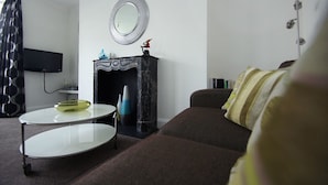 A living room with a sofa, a round coffee table, a fireplace, and a flat-screen TV mounted on the wall. - New Steine Apartment Sea View by Brighton Holiday Lets (Brighton)