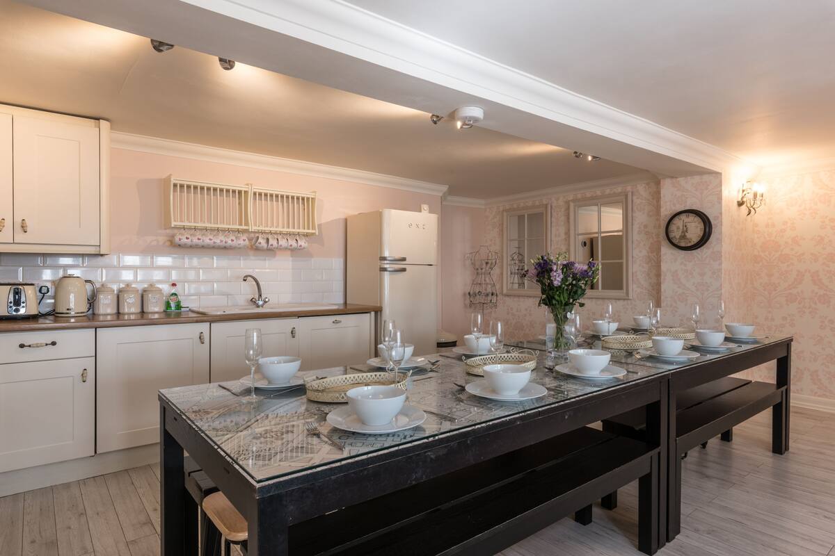 A modern kitchen with a marble countertop, white cabinetry, and a dining area set for six.