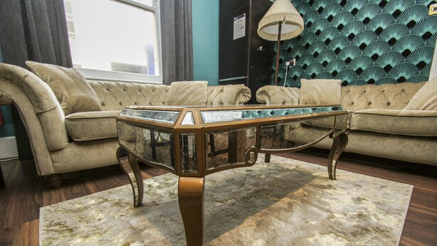 Ein Wohnzimmer mit einer gepolsterten Couch, einem Couchtisch mit Glasplatte und einem gemusterten Teppich.