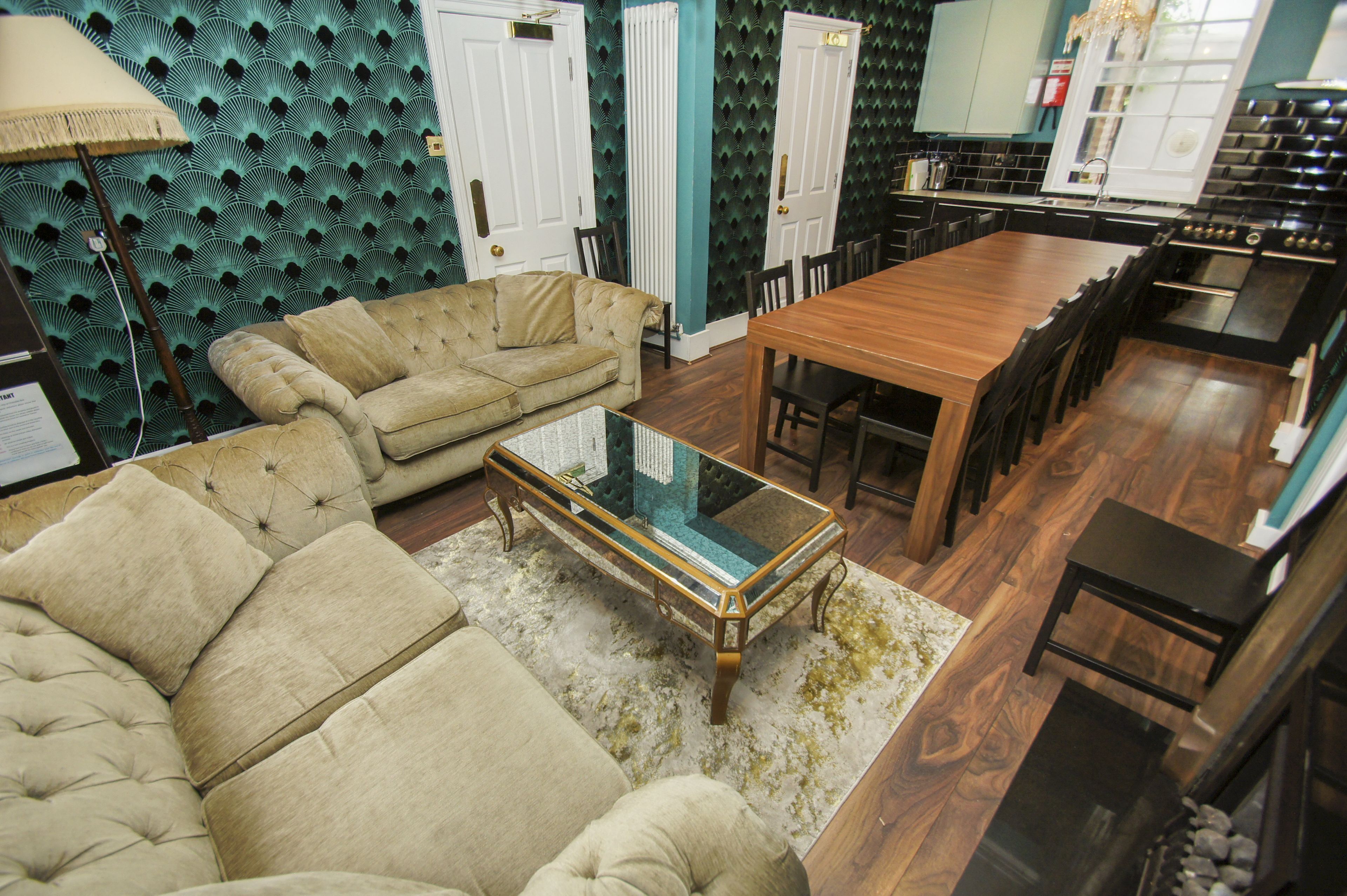 A cozy living room with a beige sofa, a glass coffee table, and a patterned wall.