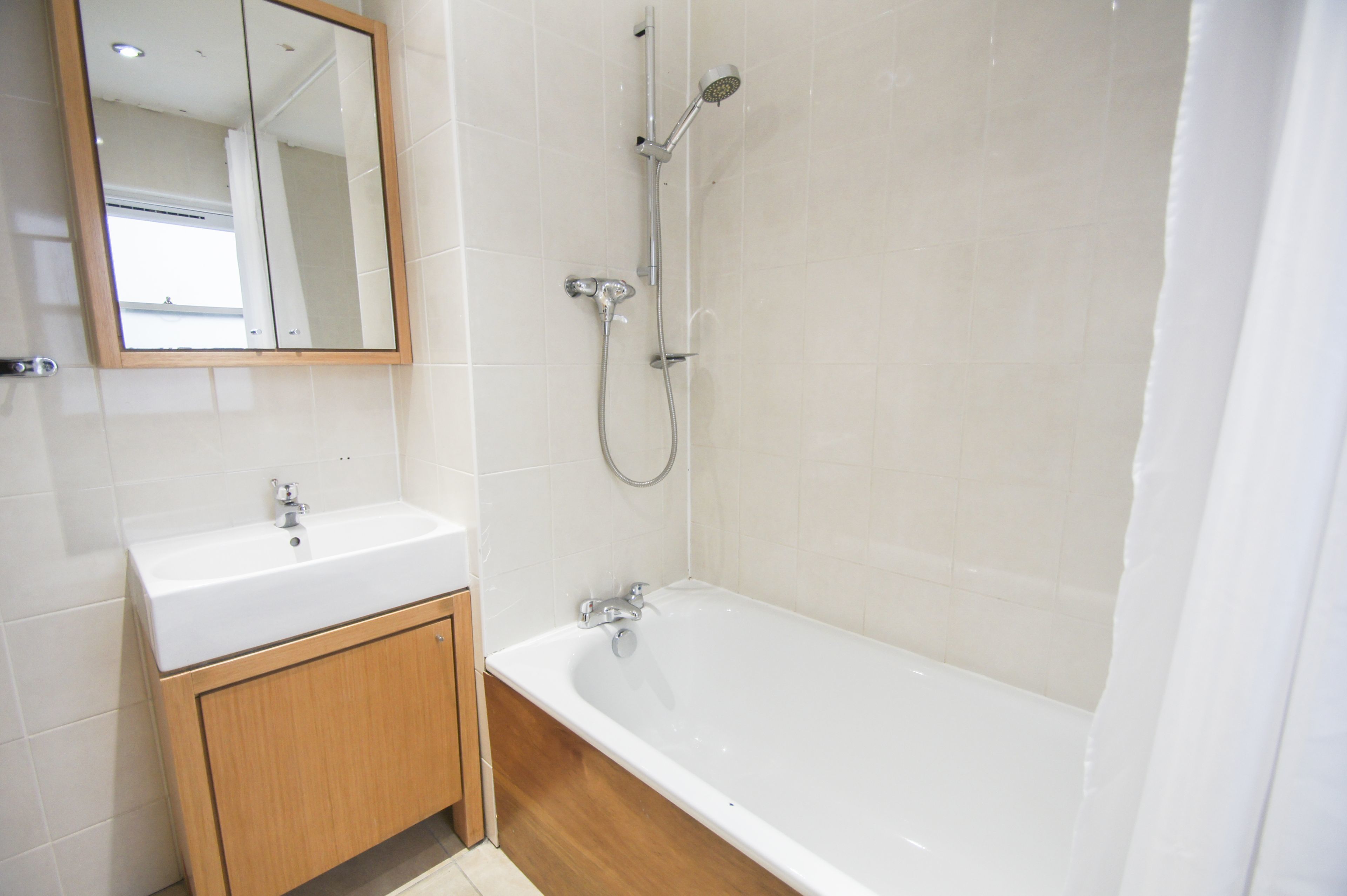 A bathroom with a white sink, wooden cabinet, and a bathtub.