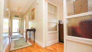 A hallway with wooden flooring, a fire exit sign, a door with frosted glass panels, and a small table with a mirror. - Dean Court Garden Parking by Brighton Holiday Lets (Brighton)