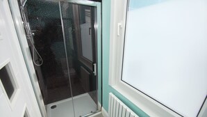 Casa de banho com cabine de duche em vidro, porta branca e radiador branco.