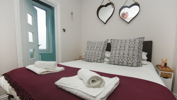 Um quarto com uma cama, dois espelhos em formato de coração e uma porta.