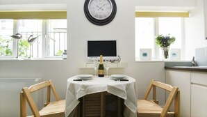 Un comedor con una mesa dispuesta para dos, un reloj de pared y un televisor sobre la mesa.